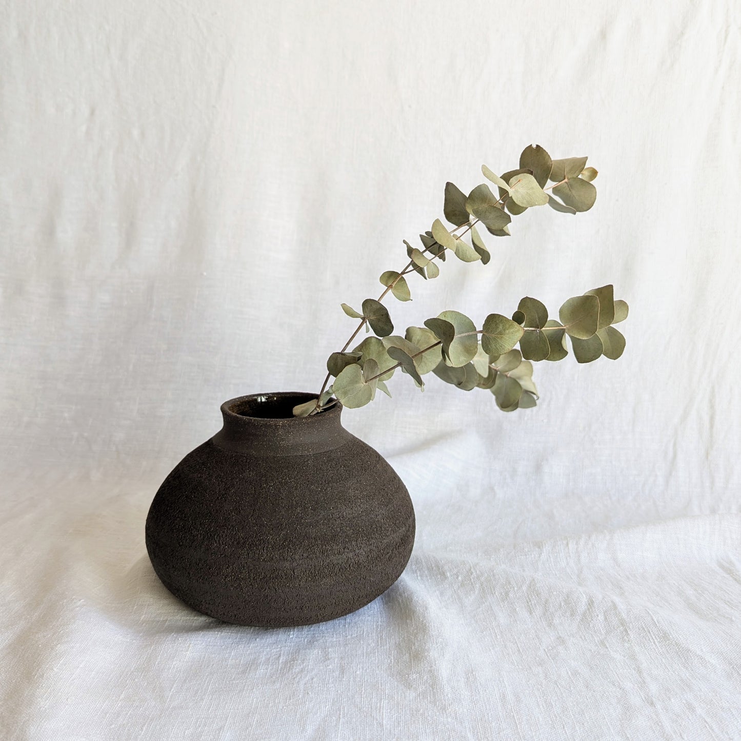 Pieza decorativa en gres negro artesanal, exterior mate con textura granulada y interior esmaltado brillante, 19 × 19 × 13 cm.