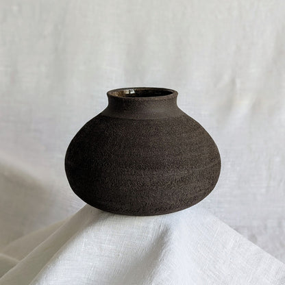 Pieza decorativa en gres negro artesanal, exterior mate con textura granulada y interior esmaltado brillante, 19 × 19 × 13 cm.