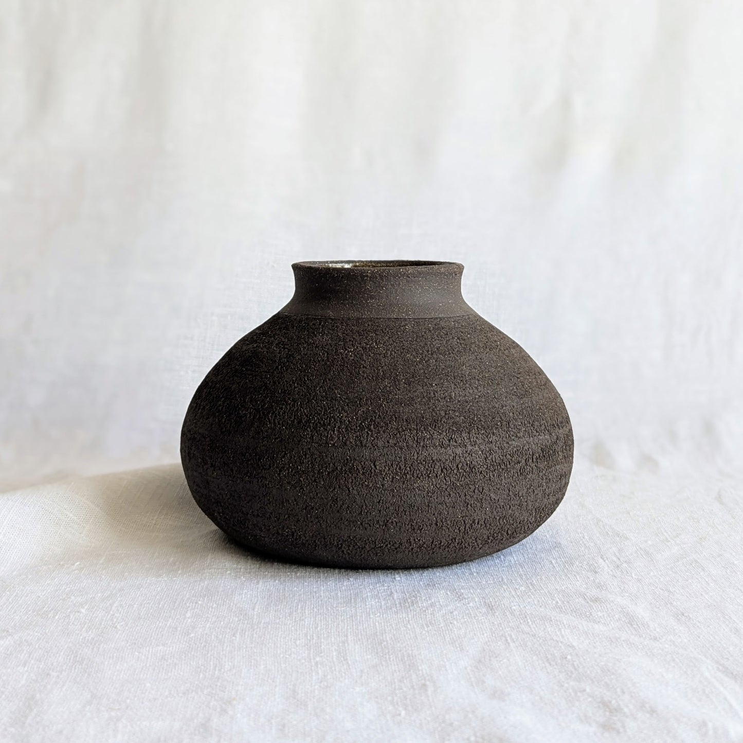 Pieza decorativa en gres negro artesanal, exterior mate con textura granulada y interior esmaltado brillante, 19 × 19 × 13 cm.