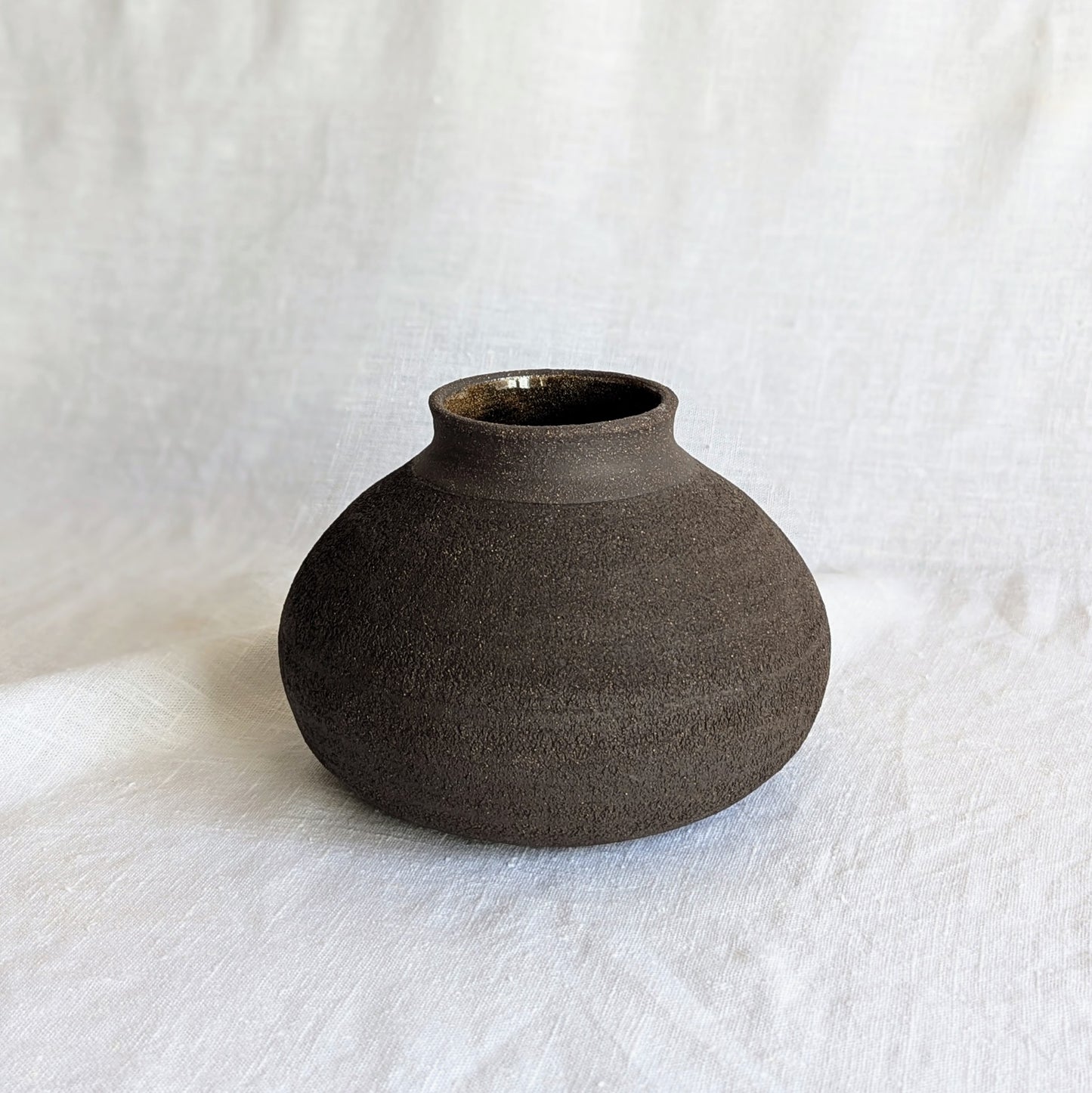 Pieza decorativa en gres negro artesanal, exterior mate con textura granulada y interior esmaltado brillante, 19 × 19 × 13 cm.