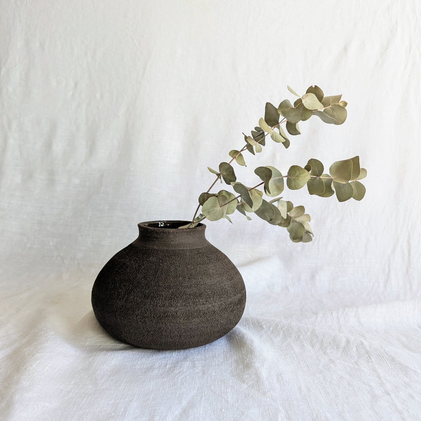 Pieza decorativa en gres negro artesanal, exterior mate con textura granulada y interior esmaltado brillante, 19 × 19 × 13 cm.