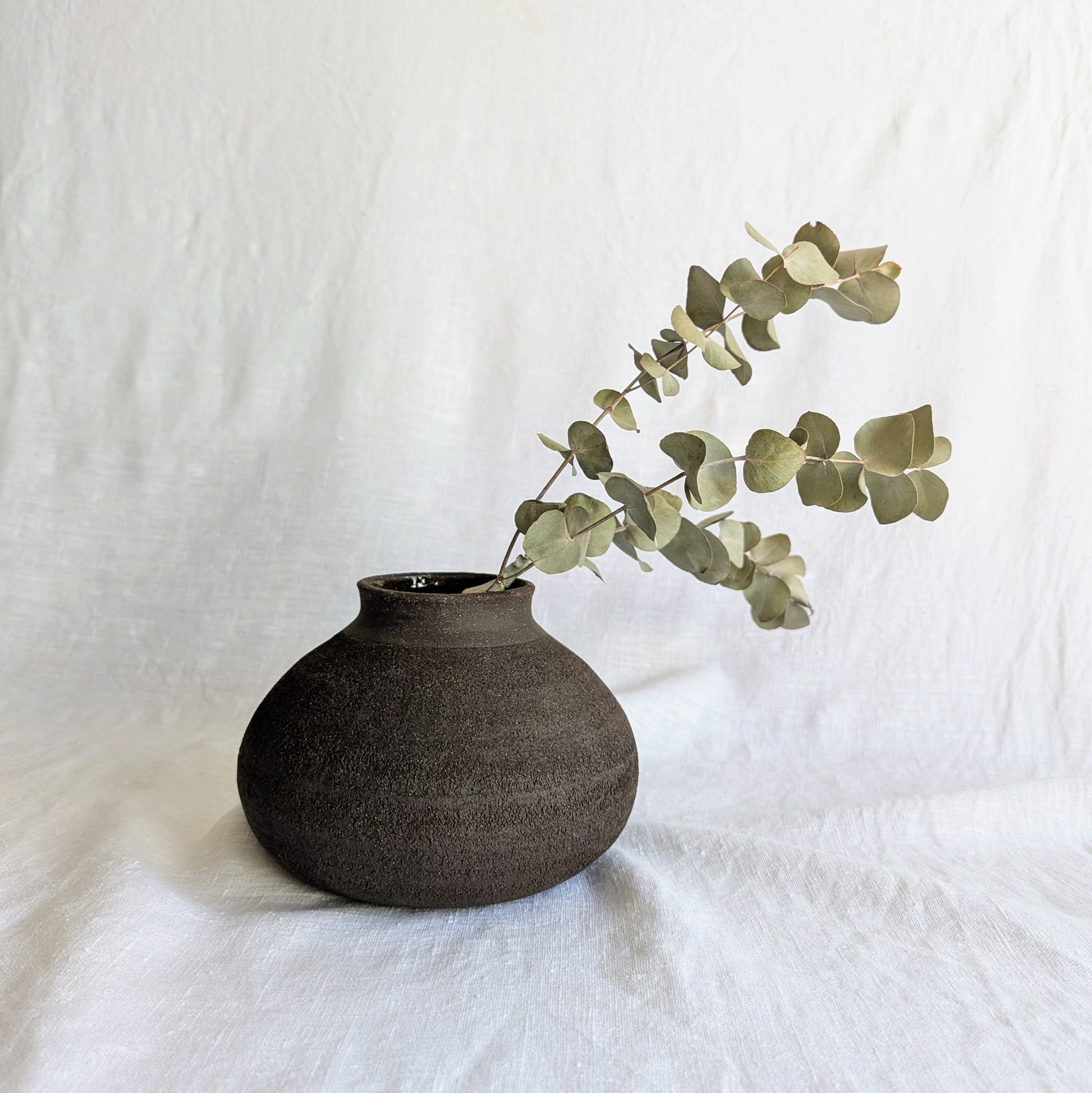 Pieza decorativa en gres negro artesanal, exterior mate con textura granulada y interior esmaltado brillante, 19 × 19 × 13 cm.