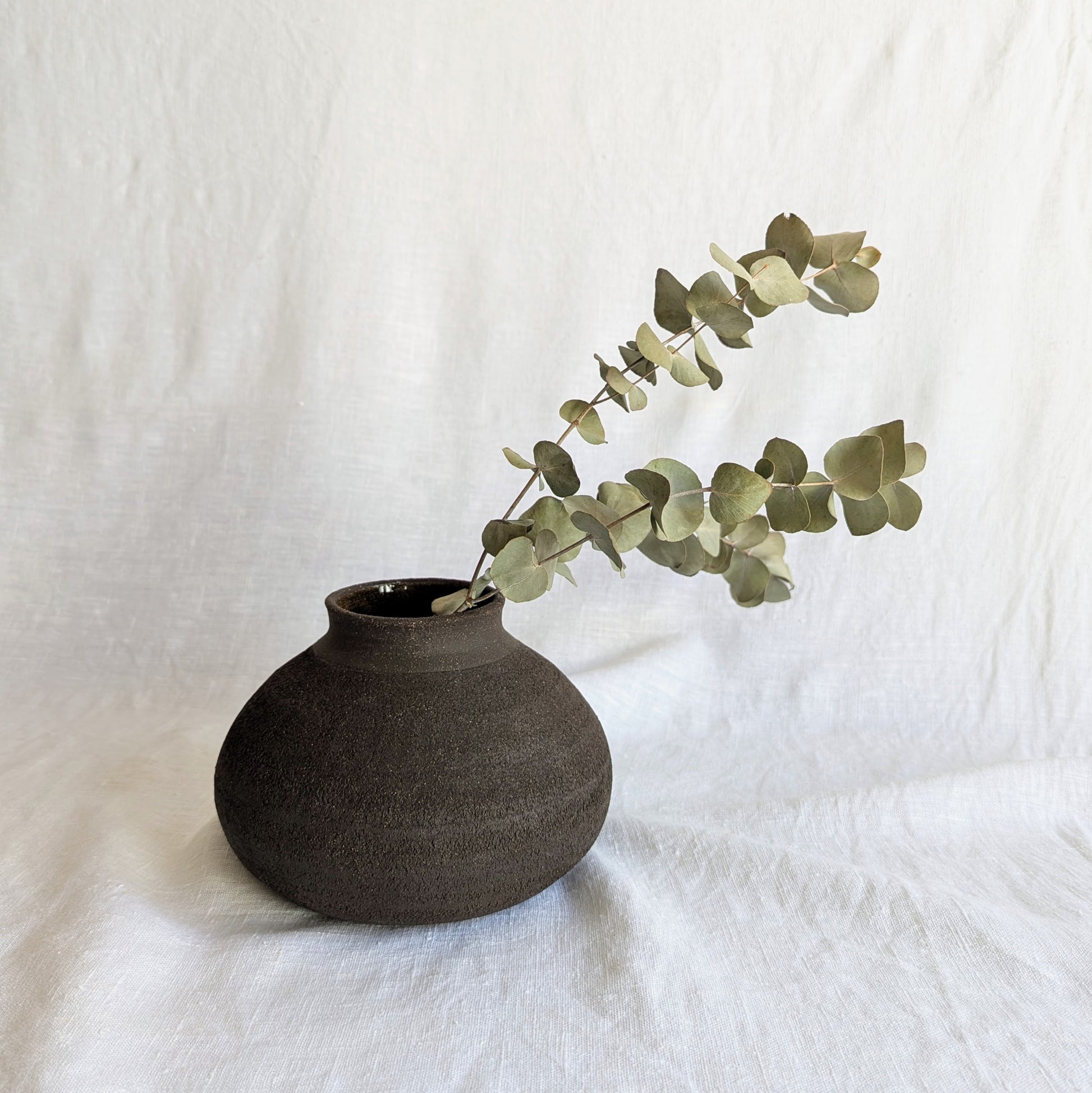 Pieza decorativa en gres negro artesanal, exterior mate con textura granulada y interior esmaltado brillante, 19 × 19 × 13 cm.