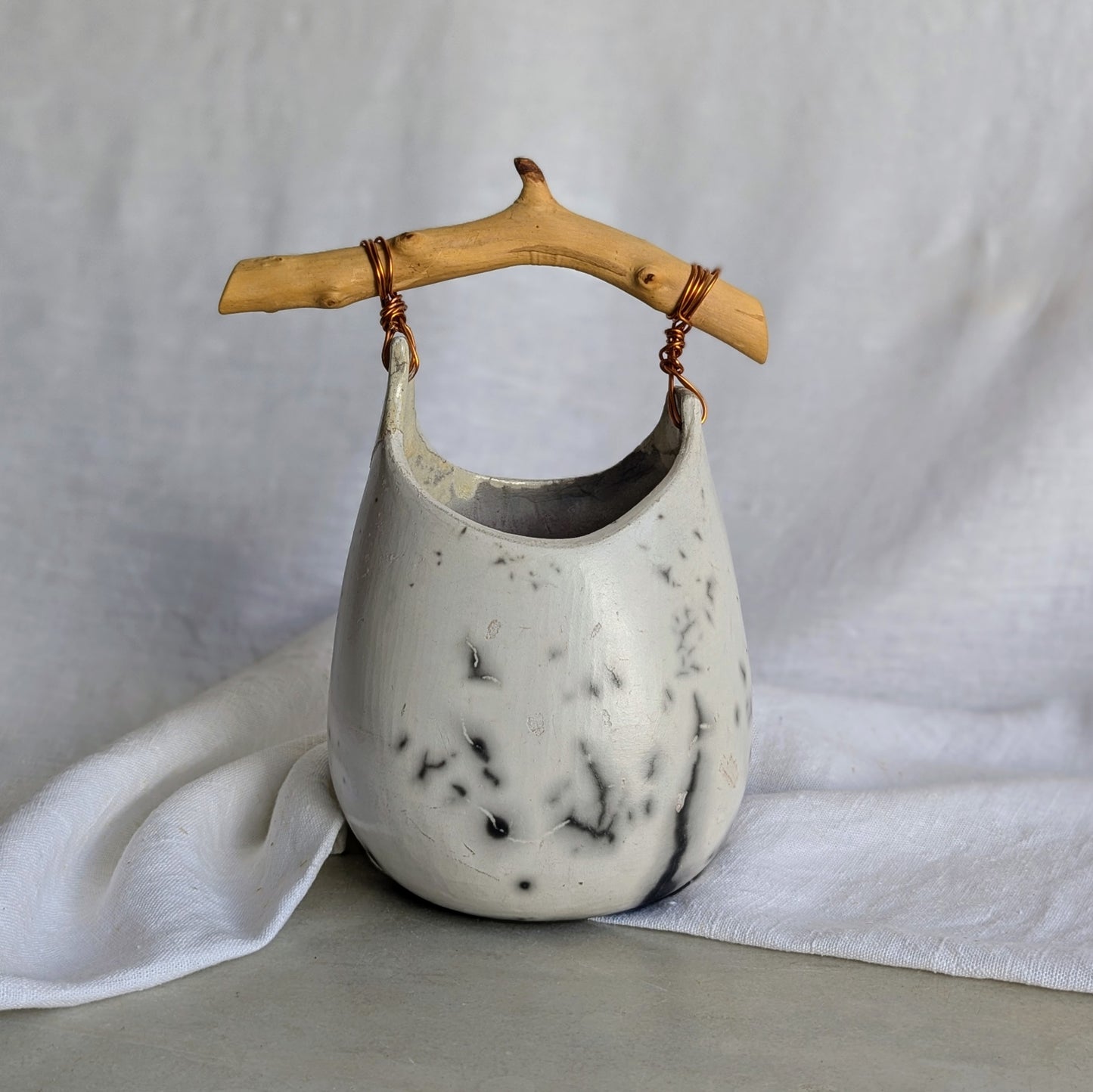 Pieza escultórica de gres blanco Rakú Naked con asa de rama de olivo y veladuras negras orgánicas, 20 × 13,5 × 26 cm.