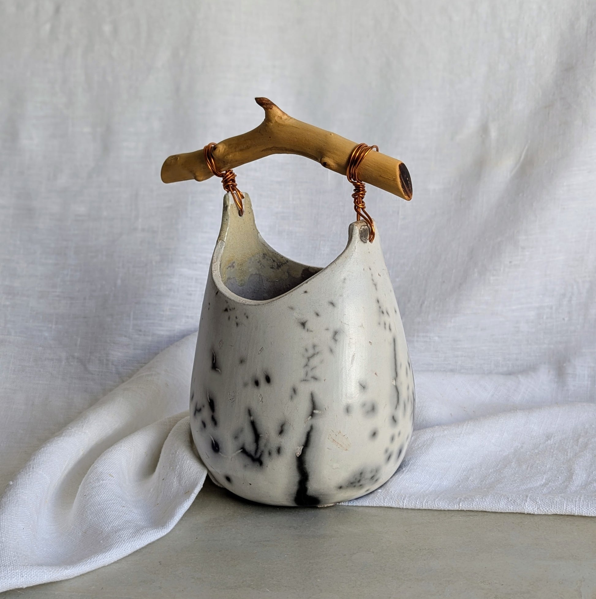 Pieza escultórica de gres blanco Rakú Naked con asa de rama de olivo y veladuras negras orgánicas, 20 × 13,5 × 26 cm.