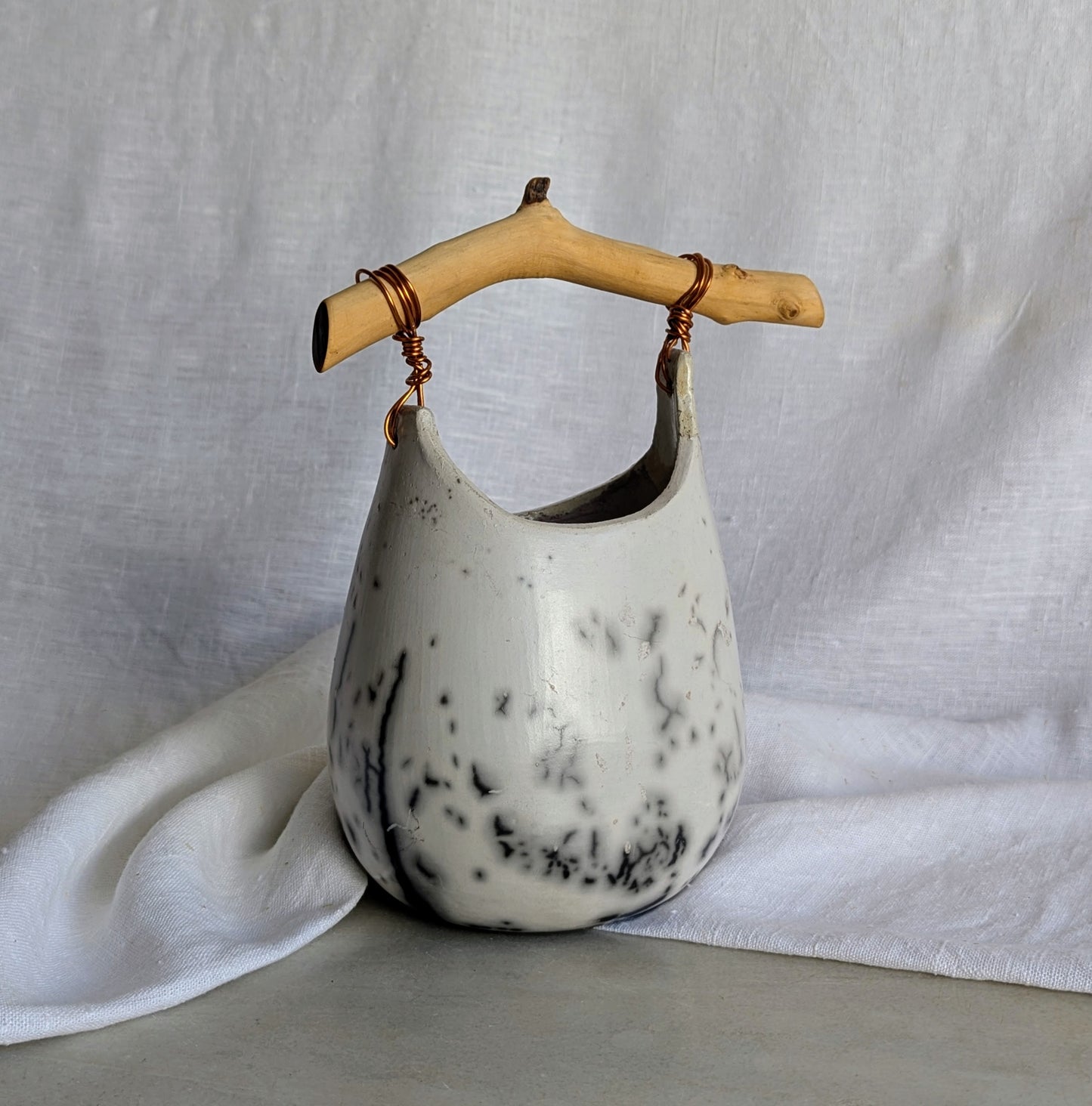 Pieza escultórica de gres blanco Rakú Naked con asa de rama de olivo y veladuras negras orgánicas, 20 × 13,5 × 26 cm.