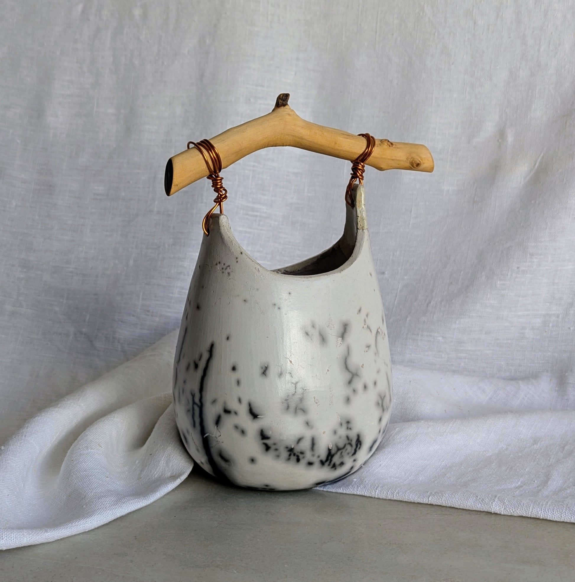 Pieza escultórica de gres blanco Rakú Naked con asa de rama de olivo y veladuras negras orgánicas, 20 × 13,5 × 26 cm.