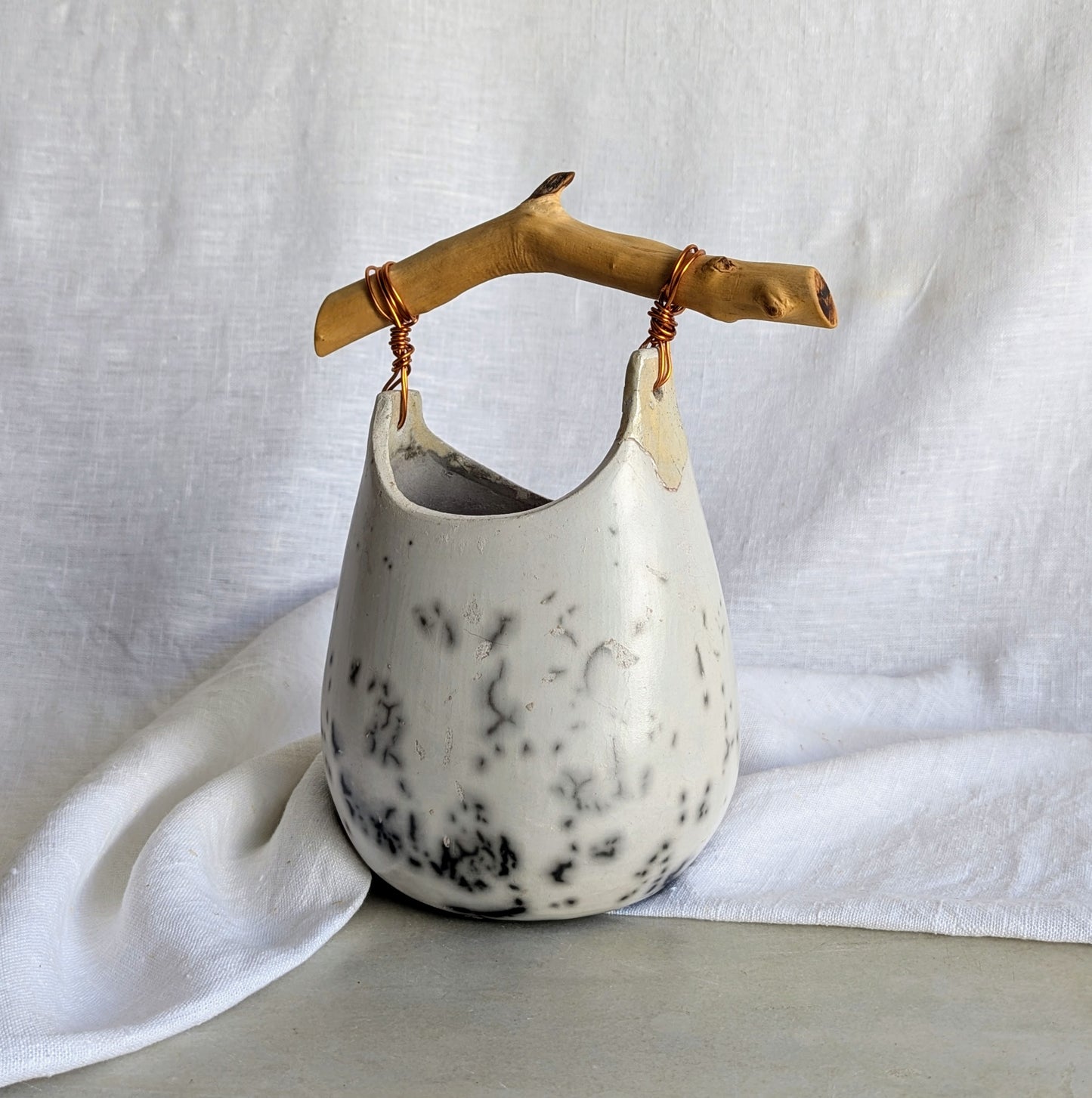 Pieza escultórica de gres blanco Rakú Naked con asa de rama de olivo y veladuras negras orgánicas, 20 × 13,5 × 26 cm.