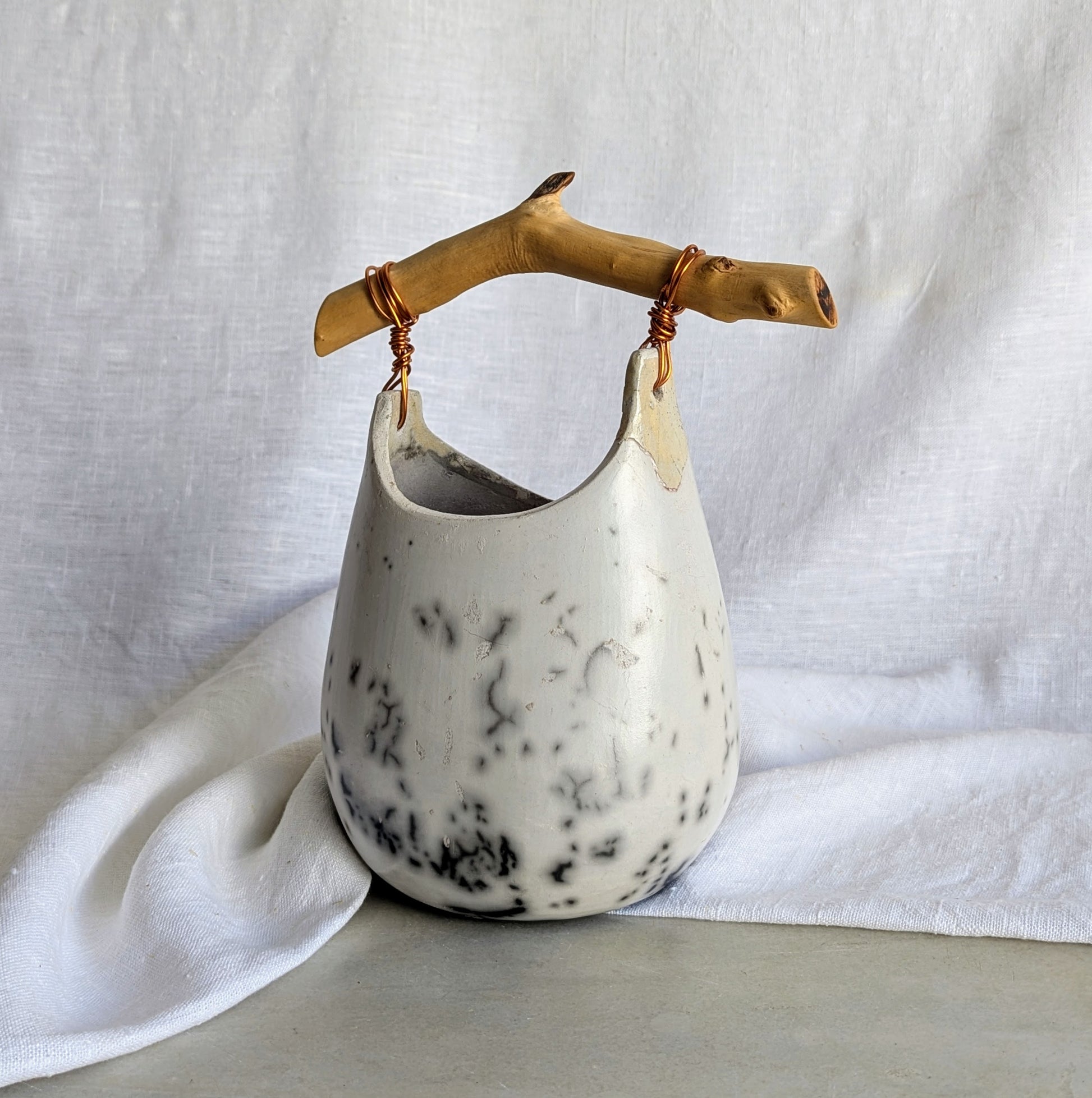 Pieza escultórica de gres blanco Rakú Naked con asa de rama de olivo y veladuras negras orgánicas, 20 × 13,5 × 26 cm.