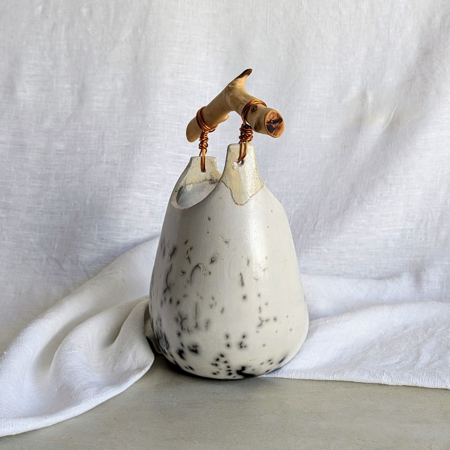 Pieza escultórica de gres blanco Rakú Naked con asa de rama de olivo y veladuras negras orgánicas, 20 × 13,5 × 26 cm.