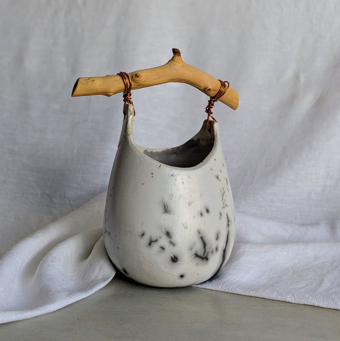 Pieza escultórica de gres blanco Rakú Naked con asa de rama de olivo y veladuras negras orgánicas, 20 × 13,5 × 26 cm.