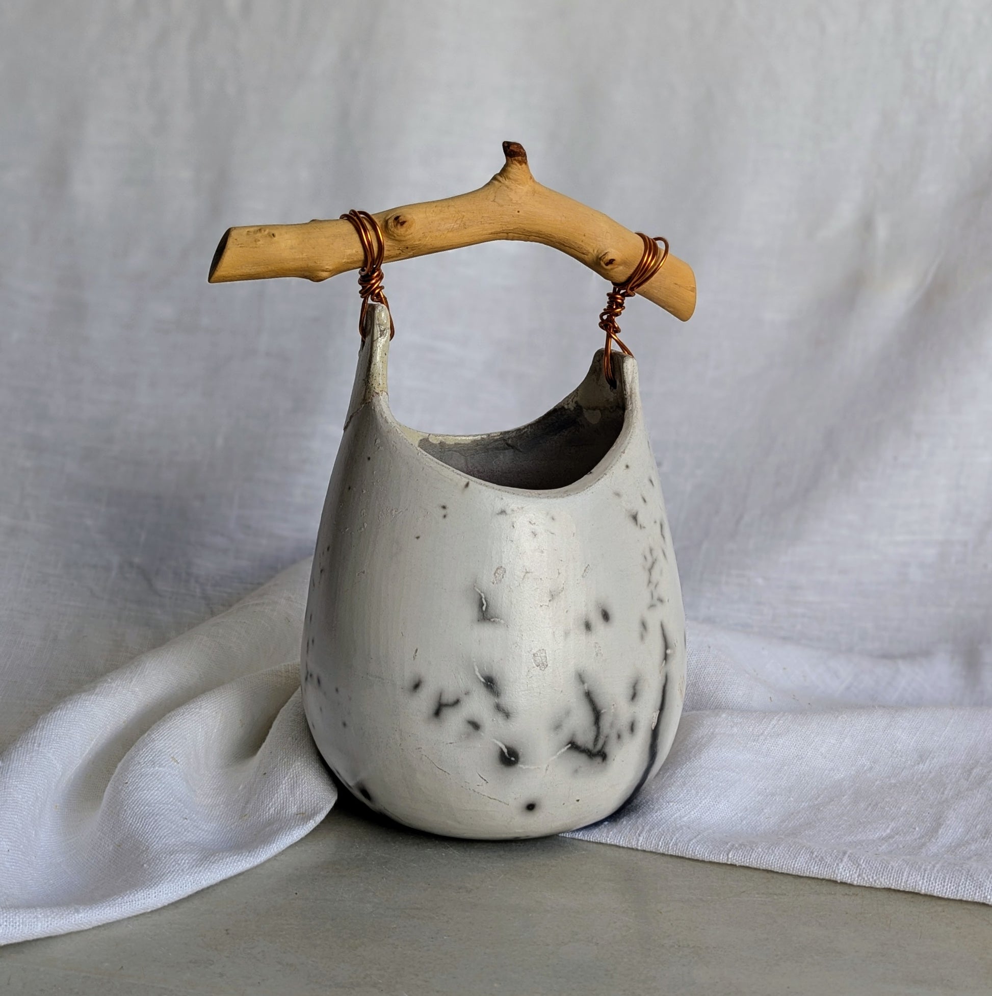 Pieza escultórica de gres blanco Rakú Naked con asa de rama de olivo y veladuras negras orgánicas, 20 × 13,5 × 26 cm.