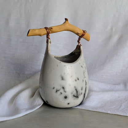 Pieza escultórica de gres blanco Rakú Naked con asa de rama de olivo y veladuras negras orgánicas, 20 × 13,5 × 26 cm.