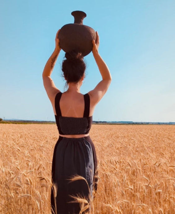 Artesana de LaLoba Cerámica sosteniendo pieza de cerámica Rakú en campo de trigo, conexión con la naturaleza y proceso artesanal